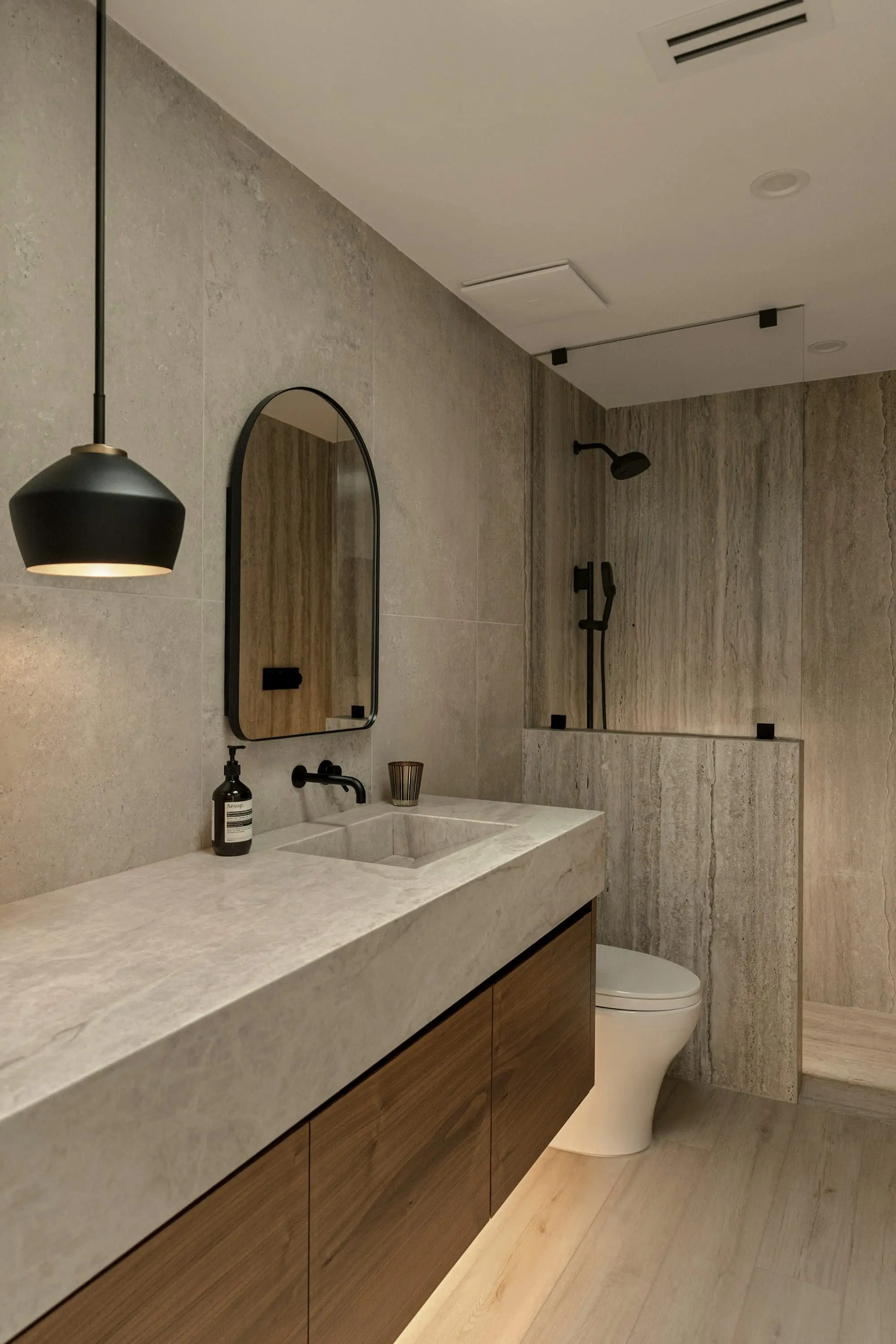 Bathroom with a stone basin counter, oak vanity and arched mirror