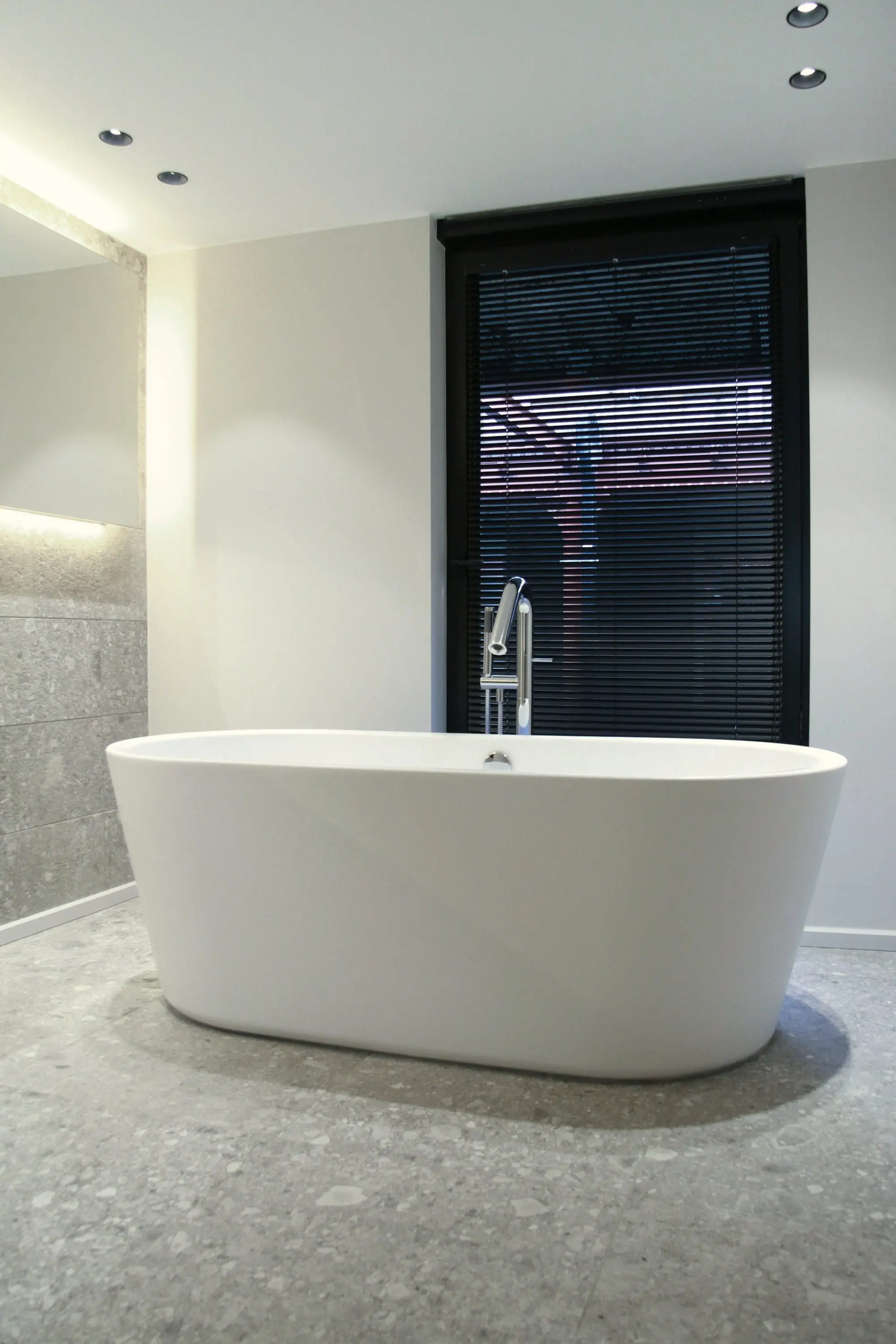 Freestanding white bath beside a dark louvred window