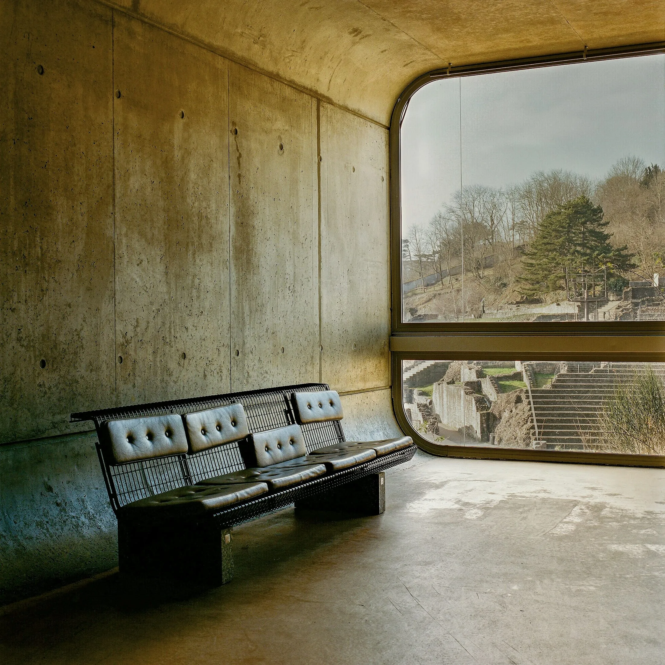 Dark leather bench beside a curved window in a concrete room