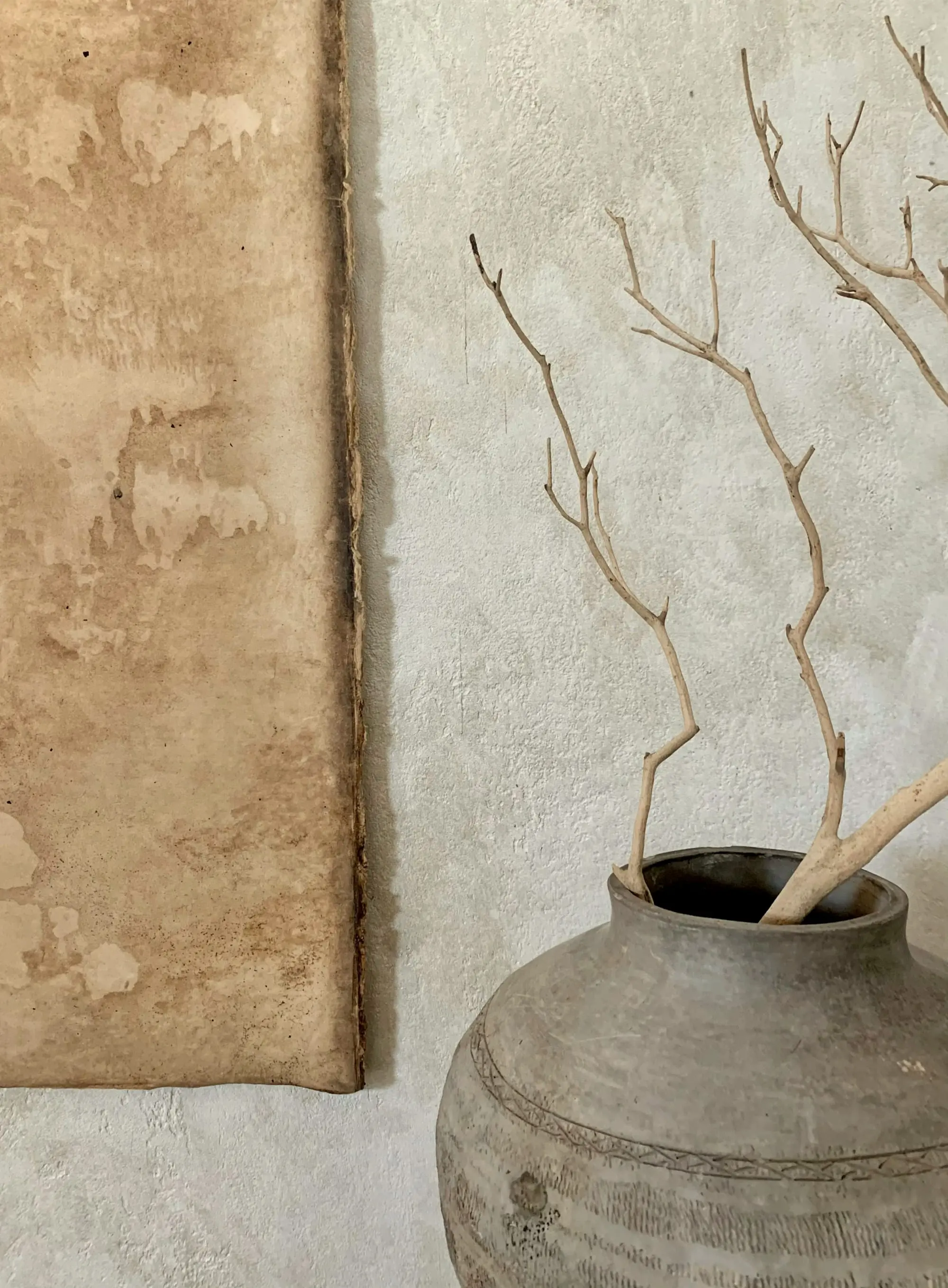 Bare branches in a stoneware pot beside an aged plaster panel
