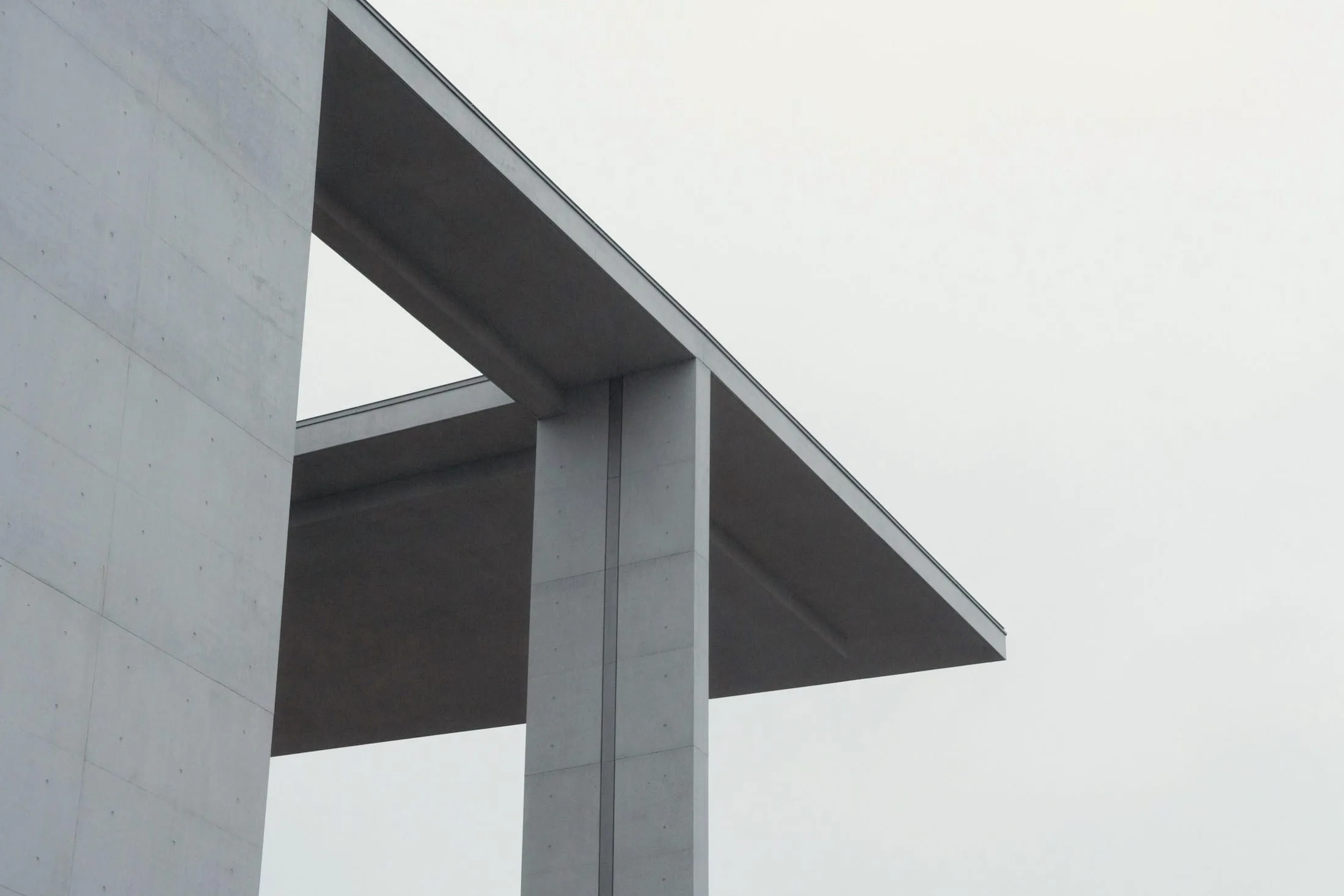Pale concrete roof plane cantilevered from a slender column against a white sky