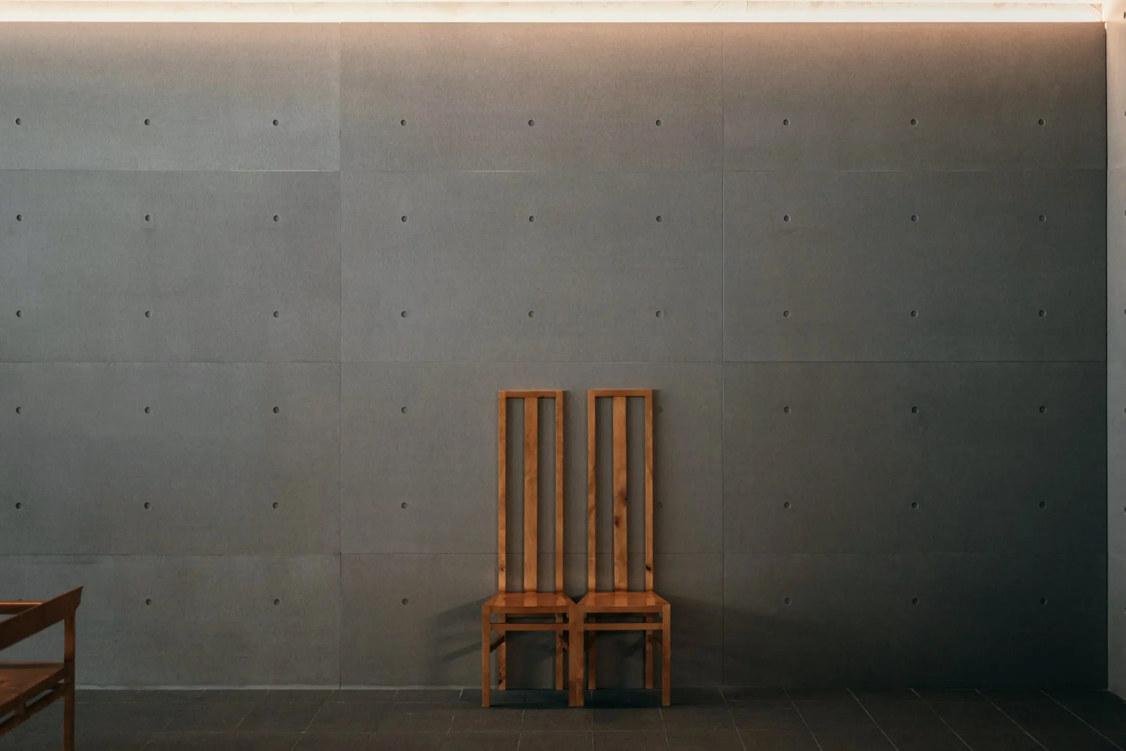 Two tall timber chairs against a dark, board-marked concrete wall