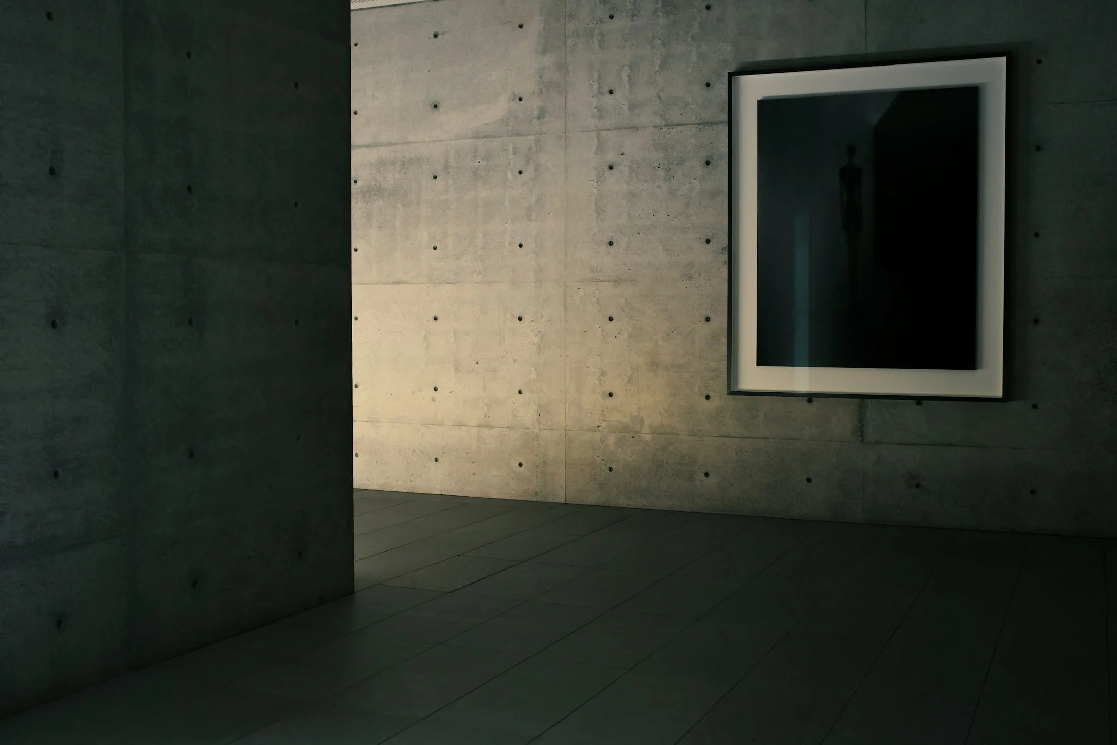 Concrete room with a black framed artwork, lit by a raking shaft of daylight