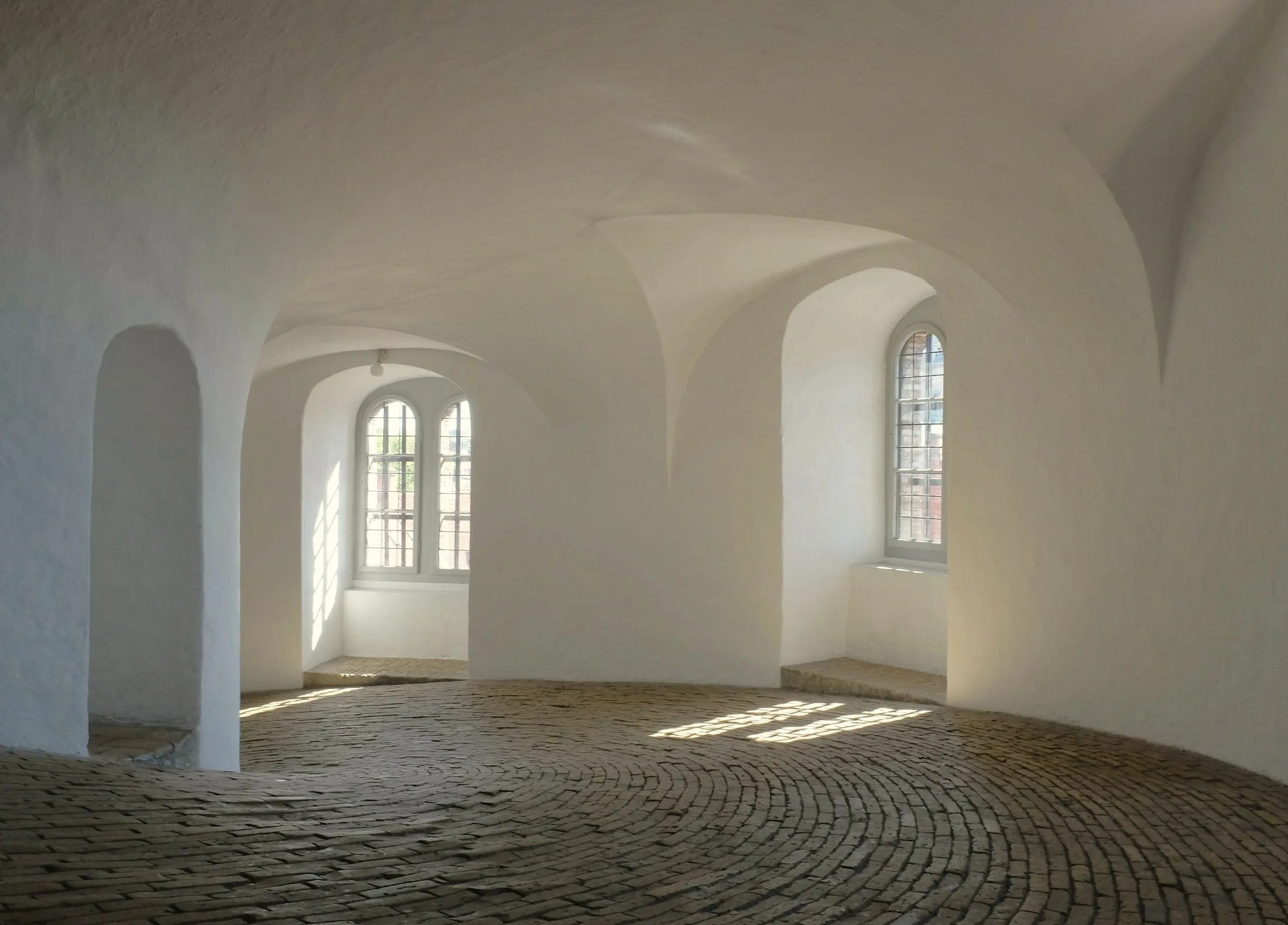 Vaulted, whitewashed room with arched windows and a brick floor